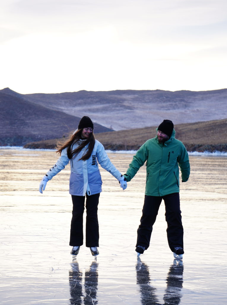 Пара держится за руки и едет на коньках на Байкале зимой